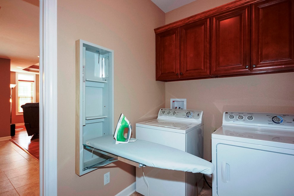 Immagine di una piccola lavanderia multiuso classica con ante con riquadro incassato, pareti beige, lavatrice e asciugatrice affiancate e ante in legno bruno