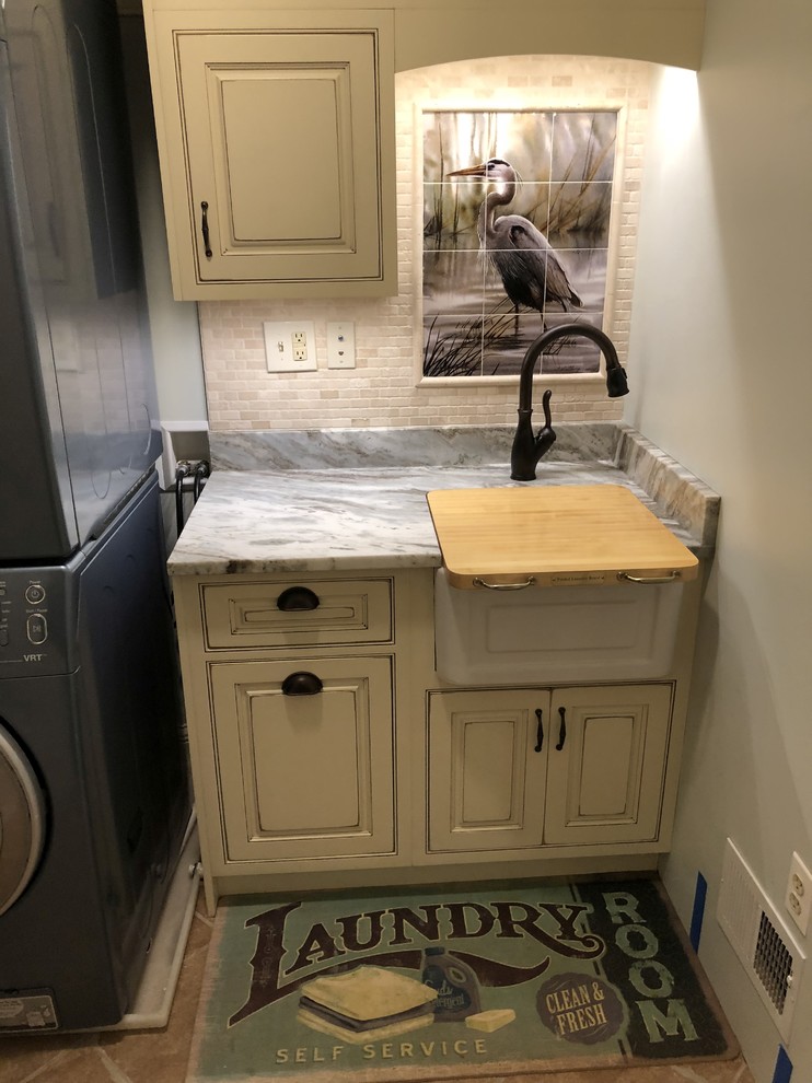 Photo of a small coastal single-wall separated utility room in Baltimore with a belfast sink, beaded cabinets, distressed cabinets, granite worktops, green walls, ceramic flooring, a stacked washer and dryer, brown floors and brown worktops.