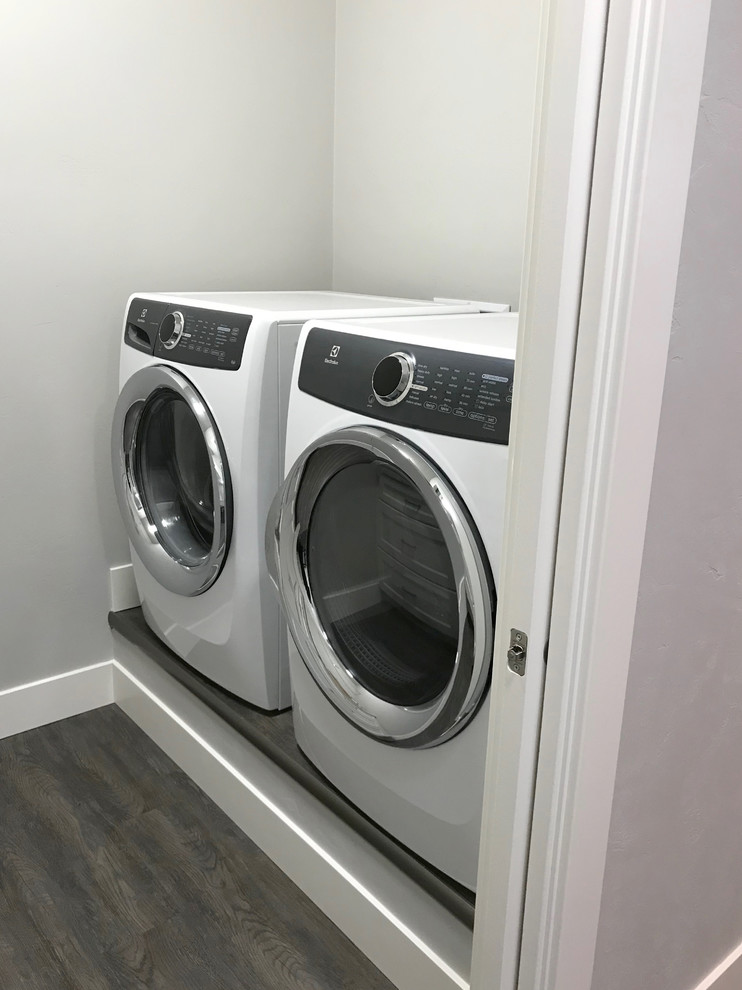 Diseño de cuarto de lavado de galera moderno pequeño con armarios estilo shaker, puertas de armario blancas, paredes blancas, suelo vinílico, lavadora y secadora juntas, suelo marrón y encimera de laminado