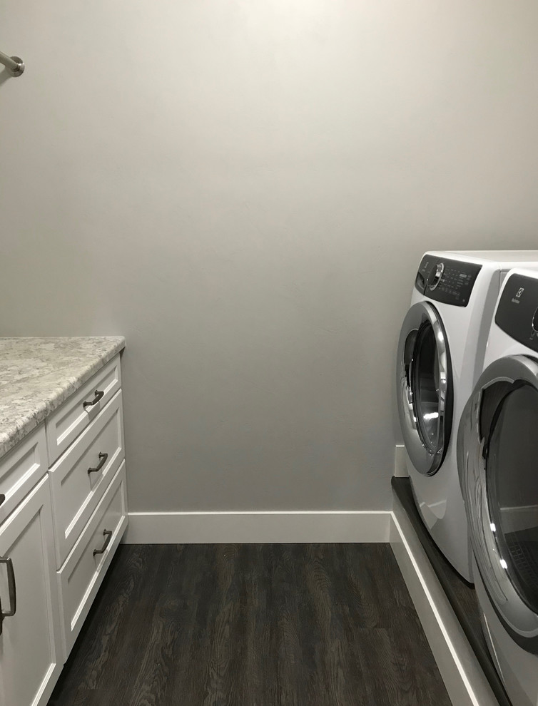 Imagen de cuarto de lavado de galera moderno pequeño con armarios estilo shaker, puertas de armario blancas, encimera de laminado, paredes blancas, suelo vinílico, lavadora y secadora juntas y suelo marrón