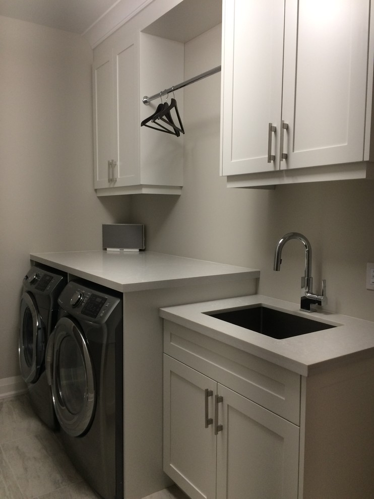 Exempel på en mellanstor modern tvättstuga, med en undermonterad diskho, skåp i shakerstil, vita skåp, beige väggar och en tvättmaskin och torktumlare bredvid varandra