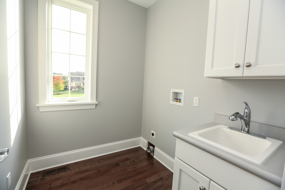 Inspiration for a medium sized classic single-wall separated utility room in New York with a built-in sink, flat-panel cabinets, white cabinets, laminate countertops, white walls, medium hardwood flooring and brown floors.