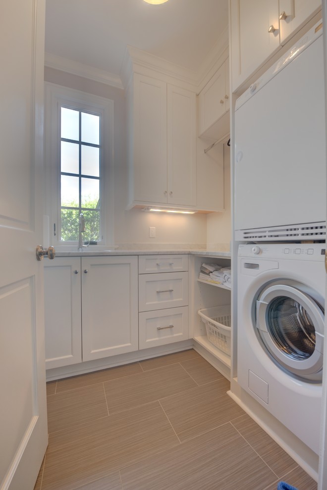 Foto de cuarto de lavado en L clásico de tamaño medio con fregadero bajoencimera, armarios con paneles empotrados, puertas de armario blancas y lavadora y secadora apiladas