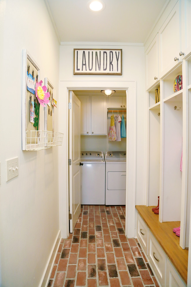 Imagen de lavadero de estilo de casa de campo con puertas de armario blancas, paredes blancas y suelo de ladrillo