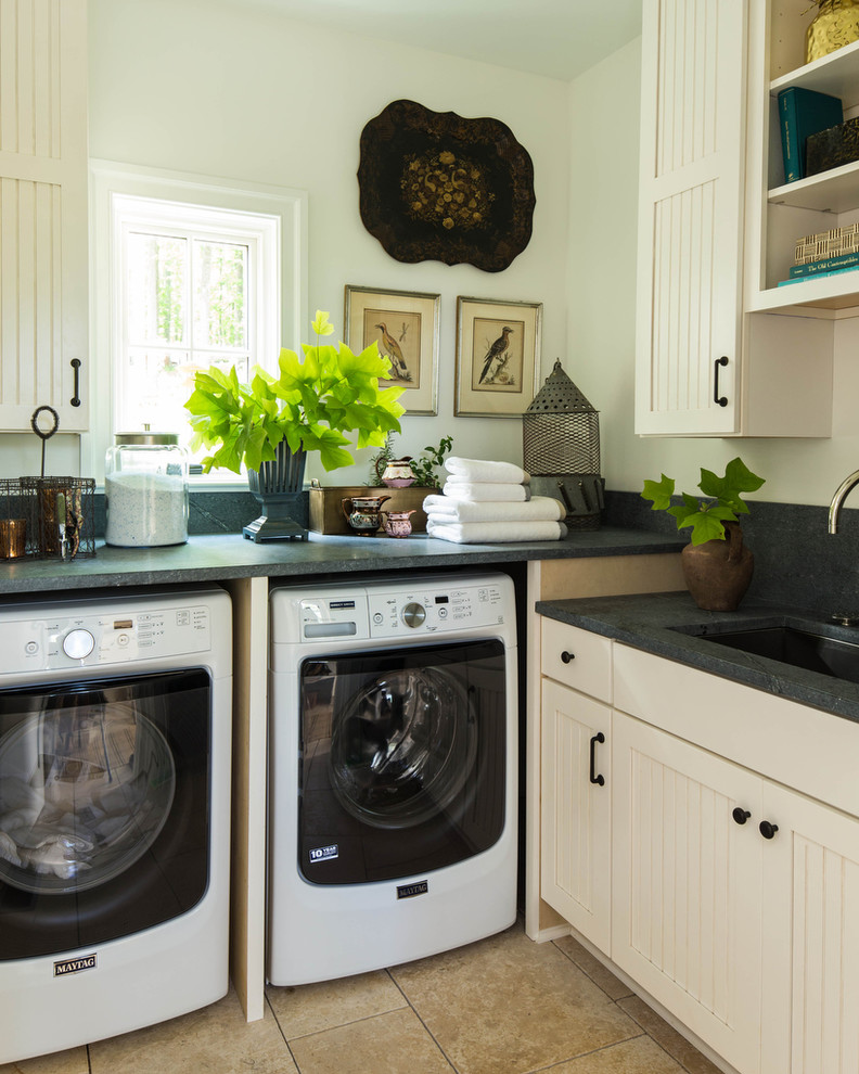 Exempel på en mellanstor lantlig l-formad tvättstuga enbart för tvätt, med skåp i shakerstil, beige skåp, en tvättmaskin och torktumlare bredvid varandra, bänkskiva i täljsten, en undermonterad diskho och vita väggar