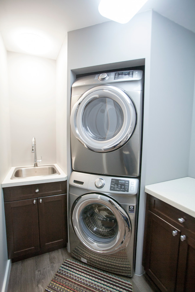 Small classic laundry cupboard in Vancouver with a submerged sink, shaker cabinets, dark wood cabinets, quartz worktops, blue walls, medium hardwood flooring and a stacked washer and dryer.