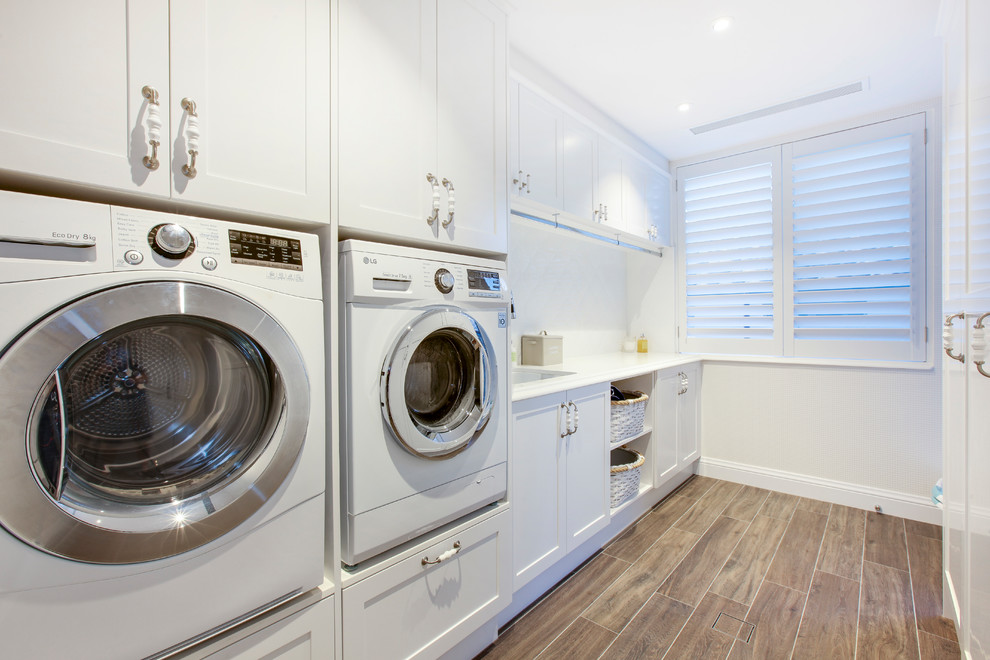 Bild på en stor funkis parallell tvättstuga enbart för tvätt, med en nedsänkt diskho, luckor med infälld panel, vita skåp, marmorbänkskiva och en tvättmaskin och torktumlare bredvid varandra