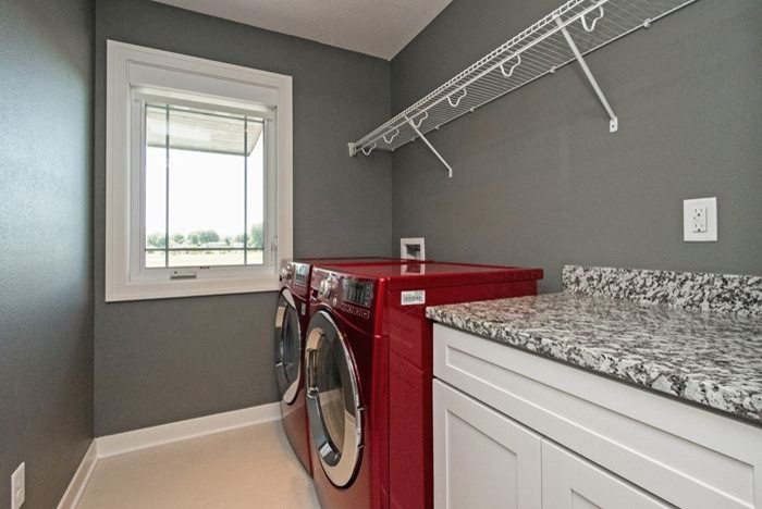 Foto på en mellanstor vintage linjär tvättstuga enbart för tvätt, med skåp i shakerstil, vita skåp, granitbänkskiva, grå väggar, klinkergolv i porslin och en tvättmaskin och torktumlare bredvid varandra