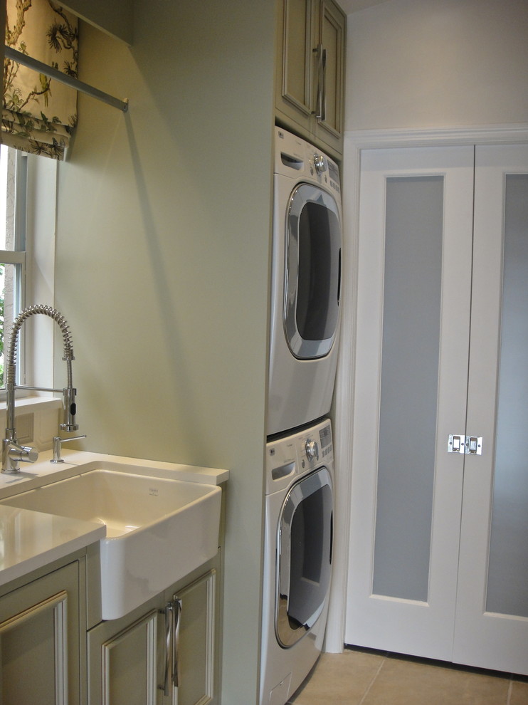 Example of a transitional galley ceramic tile dedicated laundry room design in Miami with a farmhouse sink, recessed-panel cabinets, green cabinets, quartz countertops, beige walls and a stacked washer/dryer