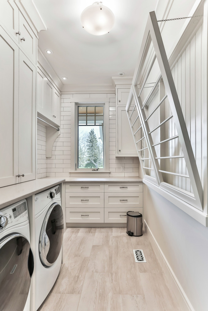 Maritime Waschküche in L-Form mit Schrankfronten im Shaker-Stil, weißen Schränken, weißer Wandfarbe, Waschmaschine und Trockner nebeneinander, beigem Boden und grauer Arbeitsplatte in Calgary