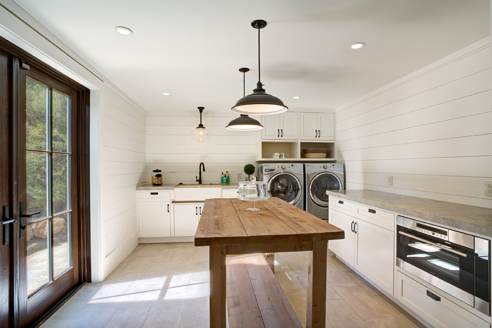 Diseño de lavadero en L campestre grande con fregadero sobremueble, puertas de armario blancas, encimera de acrílico, paredes blancas, suelo de baldosas de cerámica, lavadora y secadora juntas, suelo beige y armarios estilo shaker