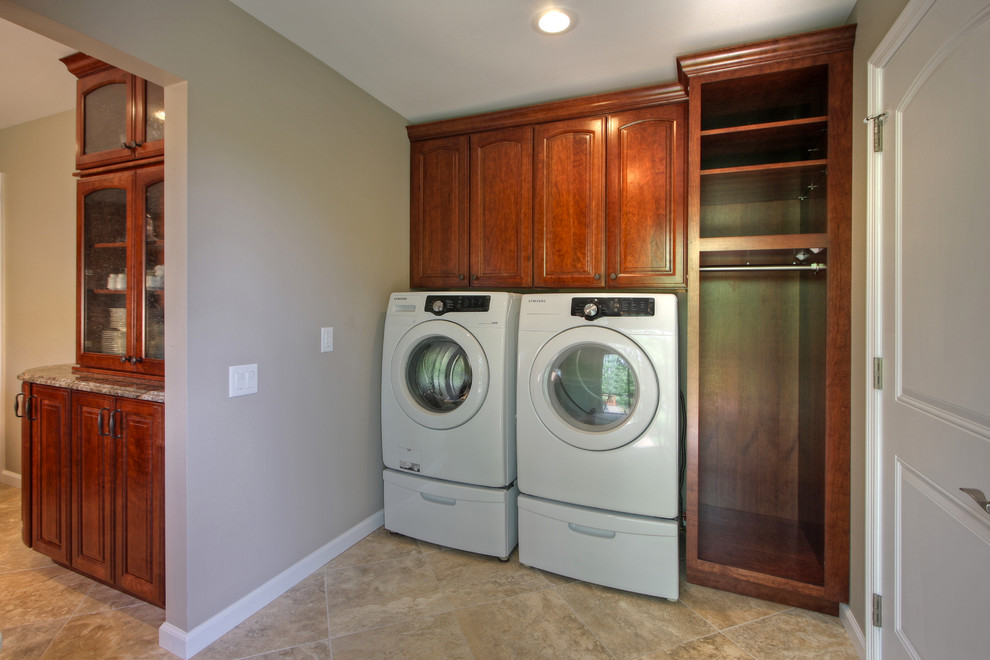 Immagine di una piccola lavanderia multiuso tradizionale con ante con riquadro incassato, pareti grigie, pavimento con piastrelle in ceramica, lavatrice e asciugatrice affiancate e ante in legno bruno