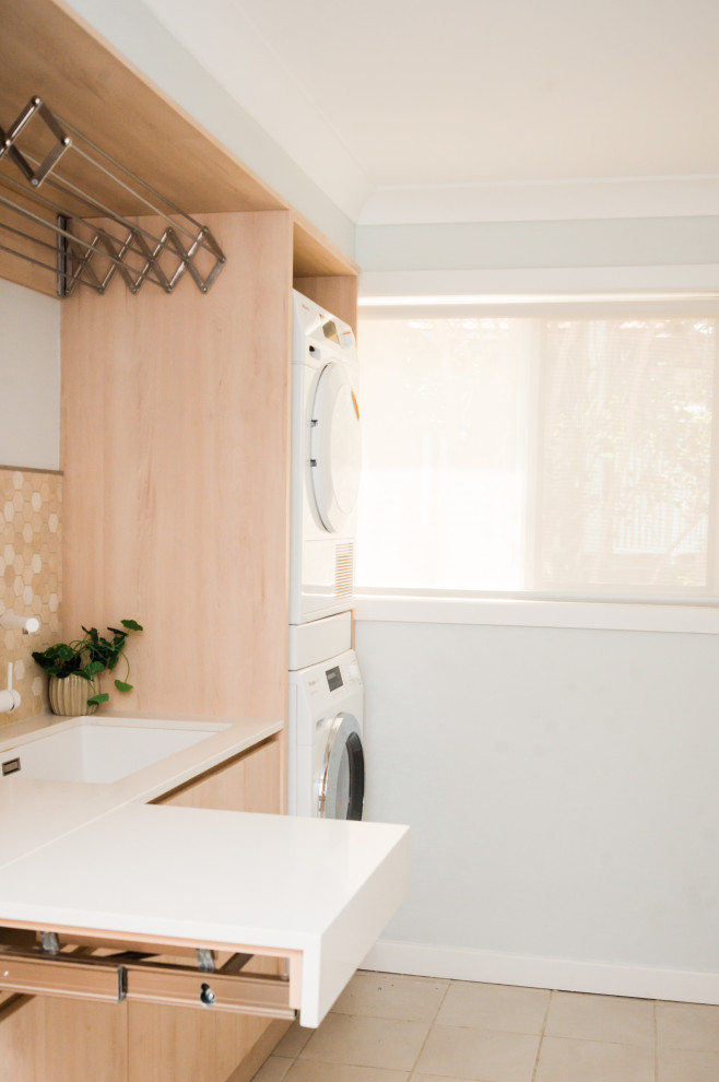 Inredning av en skandinavisk liten vita linjär vitt tvättstuga enbart för tvätt, med en undermonterad diskho, släta luckor, skåp i ljust trä, bänkskiva i kvarts, klinkergolv i porslin, en tvättpelare och brunt golv