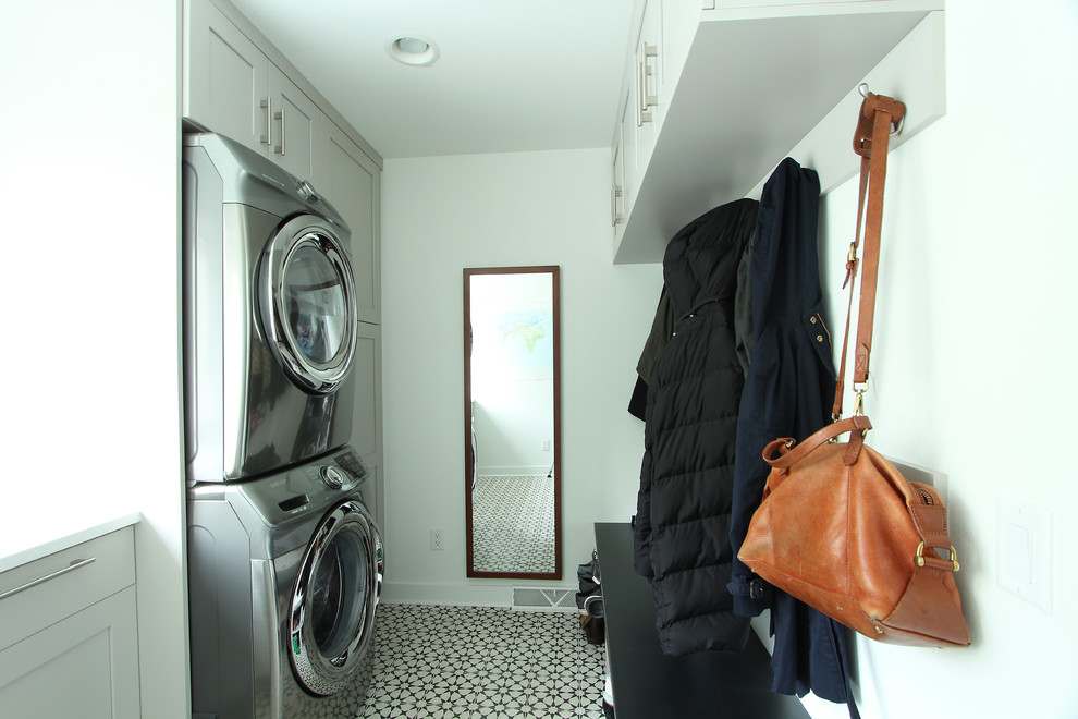 他の地域にあるお手頃価格の小さなトランジショナルスタイルのおしゃれな洗濯室 (I型、落し込みパネル扉のキャビネット、グレーのキャビネット、クオーツストーンカウンター、白い壁、磁器タイルの床、上下配置の洗濯機・乾燥機、マルチカラーの床) の写真