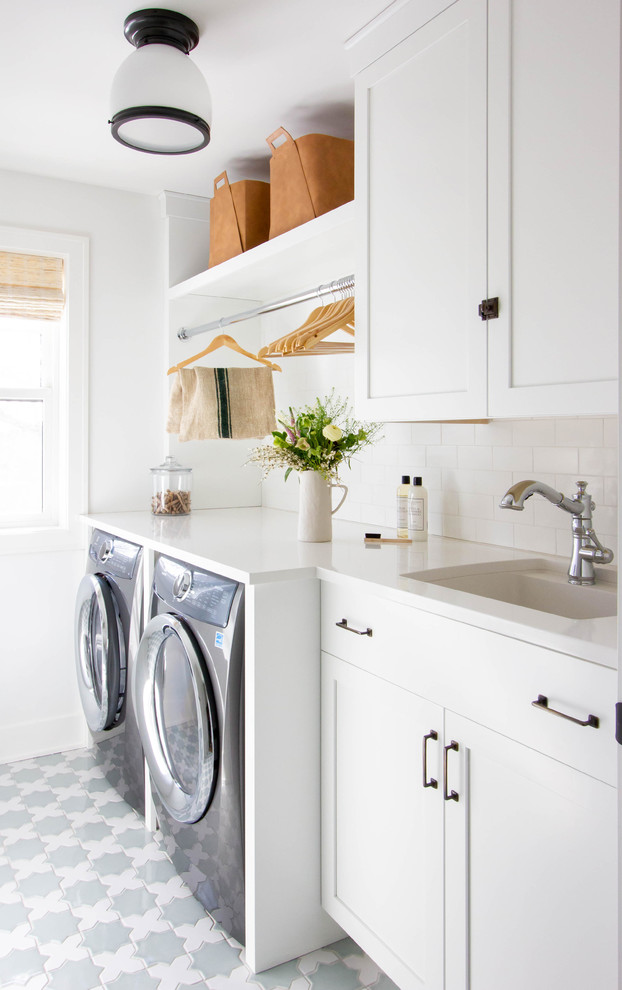 Klassisk inredning av en mellanstor vita linjär vitt tvättstuga enbart för tvätt, med vita skåp, bänkskiva i kvarts, vita väggar, klinkergolv i keramik, en tvättmaskin och torktumlare bredvid varandra, flerfärgat golv, en undermonterad diskho och skåp i shakerstil