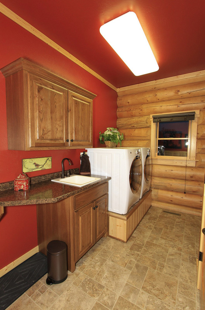 Modelo de cuarto de lavado lineal clásico con fregadero bajoencimera, armarios con paneles con relieve, puertas de armario de madera en tonos medios, paredes rojas y lavadora y secadora juntas