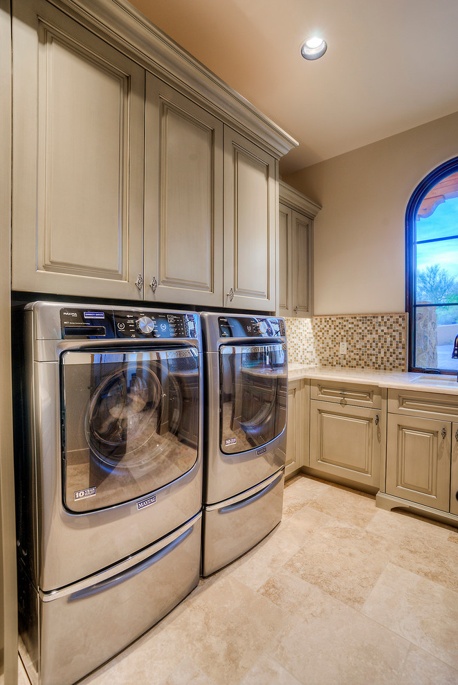 Foto di una grande sala lavanderia classica con lavello da incasso, top in granito, pareti beige, pavimento in travertino, lavatrice e asciugatrice affiancate, ante con bugna sagomata e ante grigie