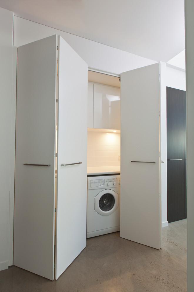 Einzeilige, Kleine Moderne Waschküche mit flächenbündigen Schrankfronten, weißen Schränken, Laminat-Arbeitsplatte, weißer Wandfarbe, Betonboden und Waschmaschine und Trockner nebeneinander in Adelaide