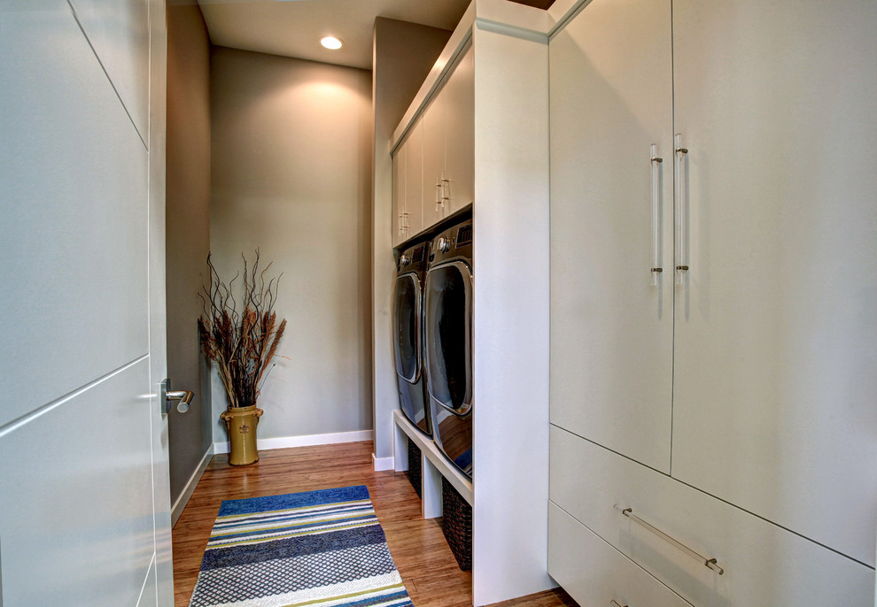 Foto de cuarto de lavado lineal contemporáneo pequeño con armarios con paneles lisos, puertas de armario blancas, paredes grises, suelo de bambú y lavadora y secadora juntas