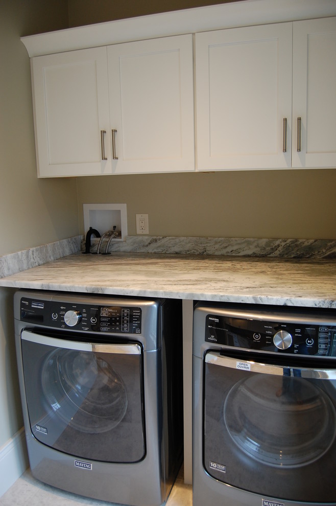 Exempel på en stor linjär tvättstuga enbart för tvätt, med vita skåp, granitbänkskiva, beige väggar, marmorgolv, en tvättmaskin och torktumlare bredvid varandra och skåp i shakerstil