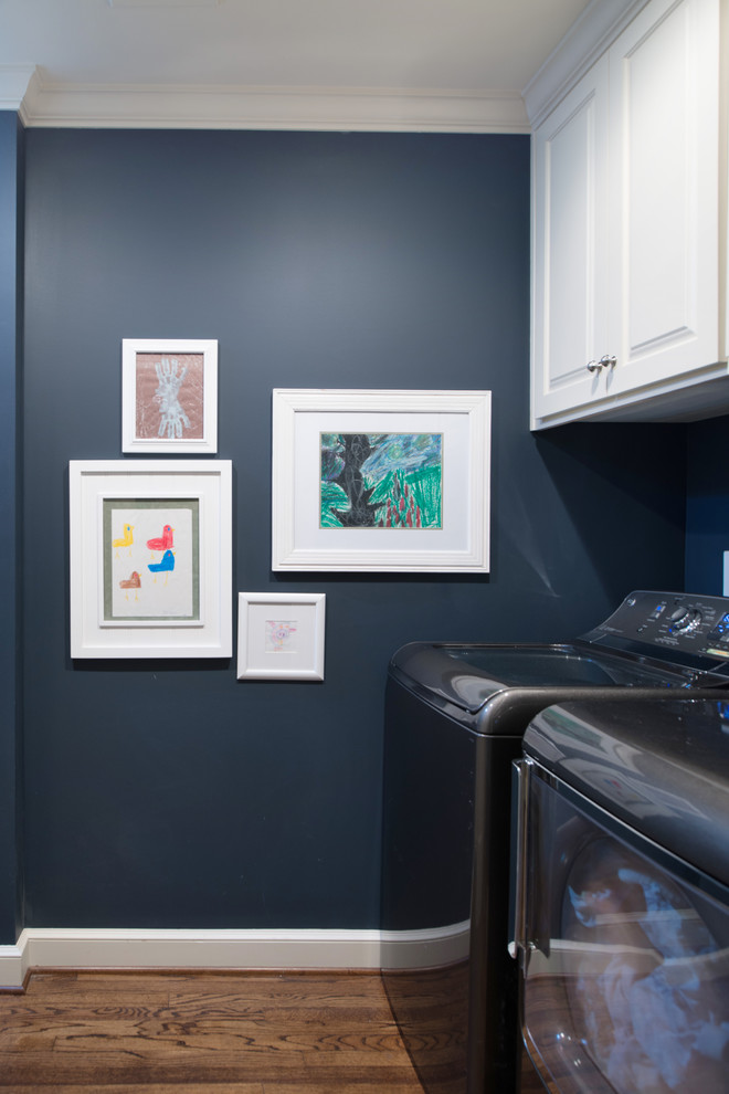 Esempio di una sala lavanderia american style di medie dimensioni con ante con bugna sagomata, ante bianche, pareti blu, pavimento in legno massello medio e lavatrice e asciugatrice affiancate