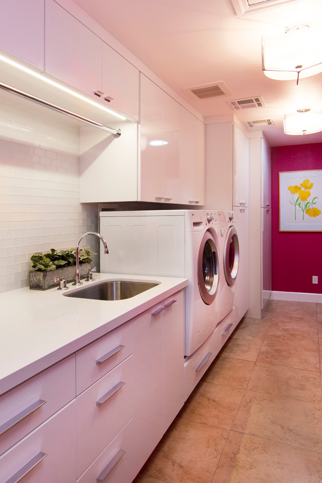ロサンゼルスにある高級な広いコンテンポラリースタイルのおしゃれな家事室 (ll型、アンダーカウンターシンク、フラットパネル扉のキャビネット、白いキャビネット、クオーツストーンカウンター、ピンクの壁、磁器タイルの床、左右配置の洗濯機・乾燥機) の写真