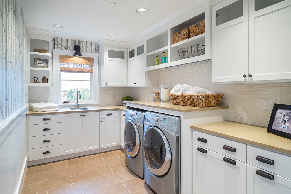 Klassische Waschküche in L-Form mit Unterbauwaschbecken, weißen Schränken, Waschmaschine und Trockner nebeneinander und beigem Boden in Portland