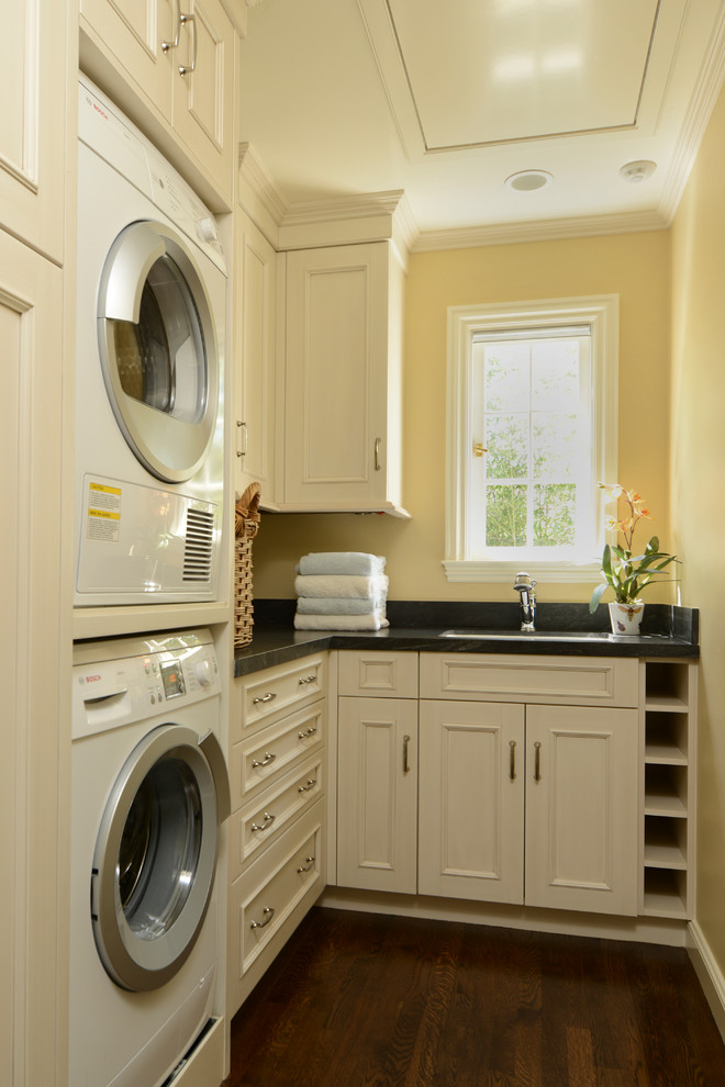 Elegant laundry room photo in San Francisco with a stacked washer/dryer, white cabinets, yellow walls and black countertops