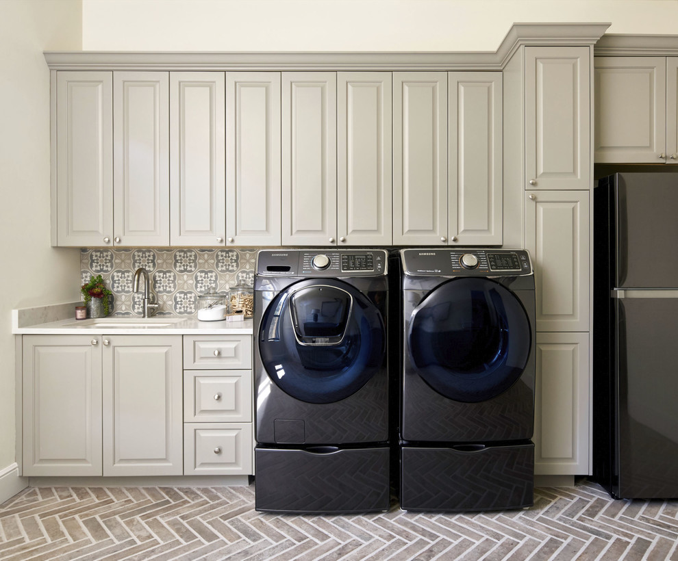Foto di un'ampia sala lavanderia classica con lavello sottopiano, ante con bugna sagomata, top in quarzo composito, lavatrice e asciugatrice affiancate, top bianco e ante beige