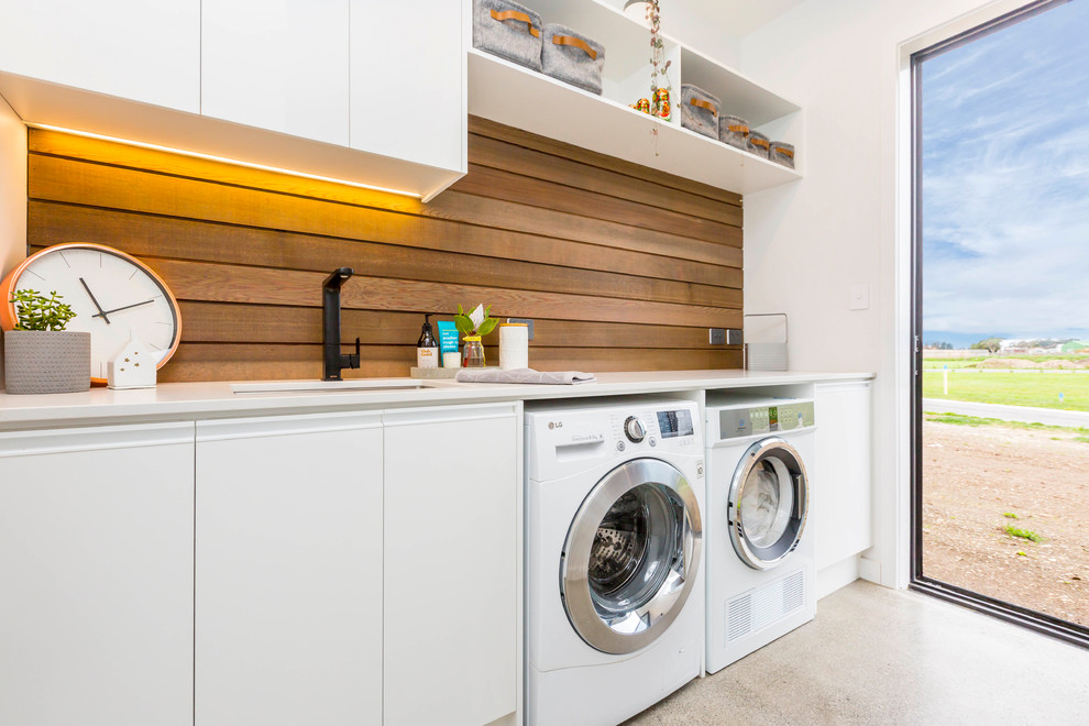 Immagine di una lavanderia design con lavello sottopiano, ante lisce, ante bianche, pavimento in cemento, lavatrice e asciugatrice affiancate, pavimento grigio e top bianco