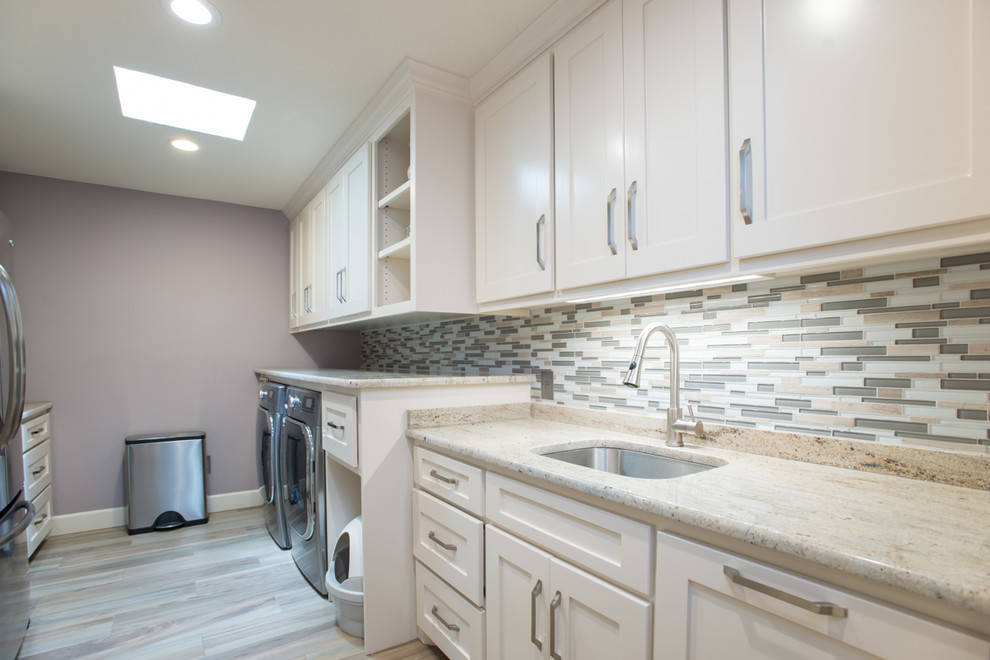 Modern inredning av en stor parallell tvättstuga enbart för tvätt, med en undermonterad diskho, skåp i shakerstil, vita skåp, granitbänkskiva, klinkergolv i porslin, en tvättmaskin och torktumlare bredvid varandra, brunt golv och grå väggar
