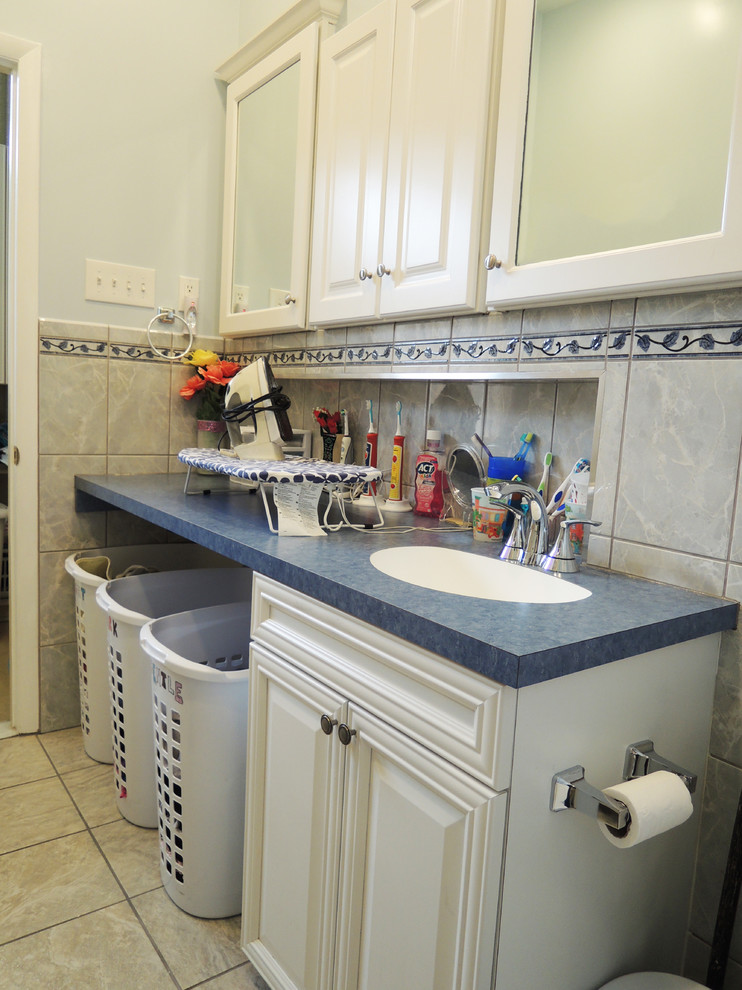 Medium sized classic u-shaped utility room in Baltimore with flat-panel cabinets, white cabinets, laminate countertops, white walls, vinyl flooring and a stacked washer and dryer.