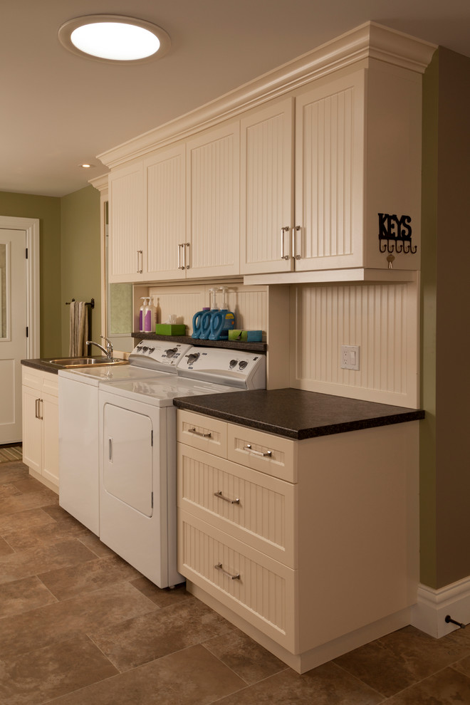 This is an example of a traditional utility room in Toronto with a built-in sink, white cabinets, green walls, ceramic flooring and a side by side washer and dryer.