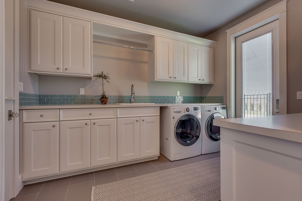 Modelo de lavadero actual de tamaño medio con fregadero encastrado, puertas de armario blancas, encimera de laminado, paredes grises, lavadora y secadora juntas y armarios con paneles empotrados