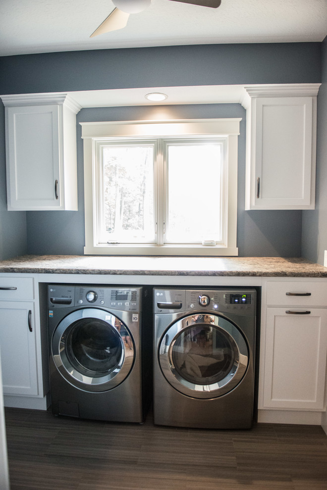 Immagine di un ripostiglio-lavanderia di medie dimensioni con ante lisce, ante bianche, top in laminato, pareti blu, pavimento in laminato, lavatrice e asciugatrice affiancate, pavimento marrone e top multicolore