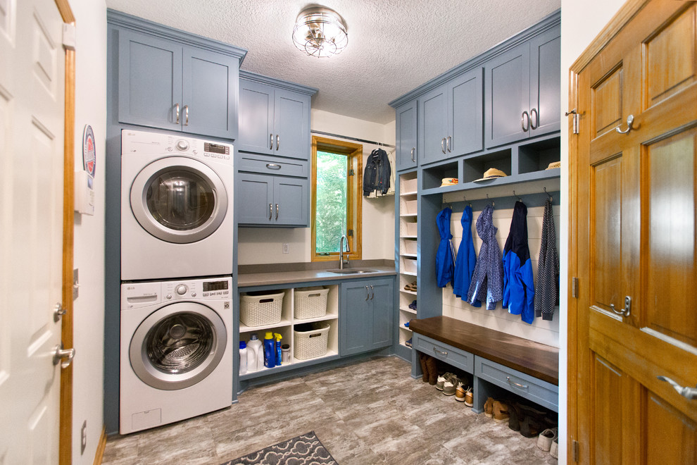 Foto de lavadero multiusos y en L clásico con fregadero bajoencimera, armarios estilo shaker, puertas de armario azules, paredes blancas, lavadora y secadora apiladas, suelo gris y encimeras grises