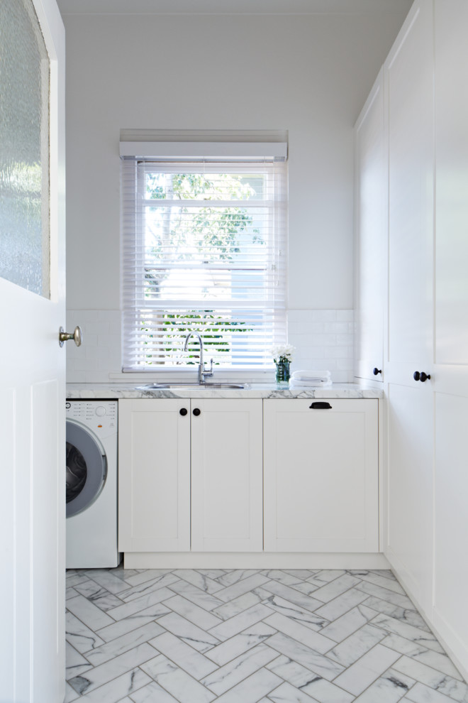 Diseño de lavadero clásico renovado con puertas de armario blancas, lavadora y secadora juntas y suelo blanco