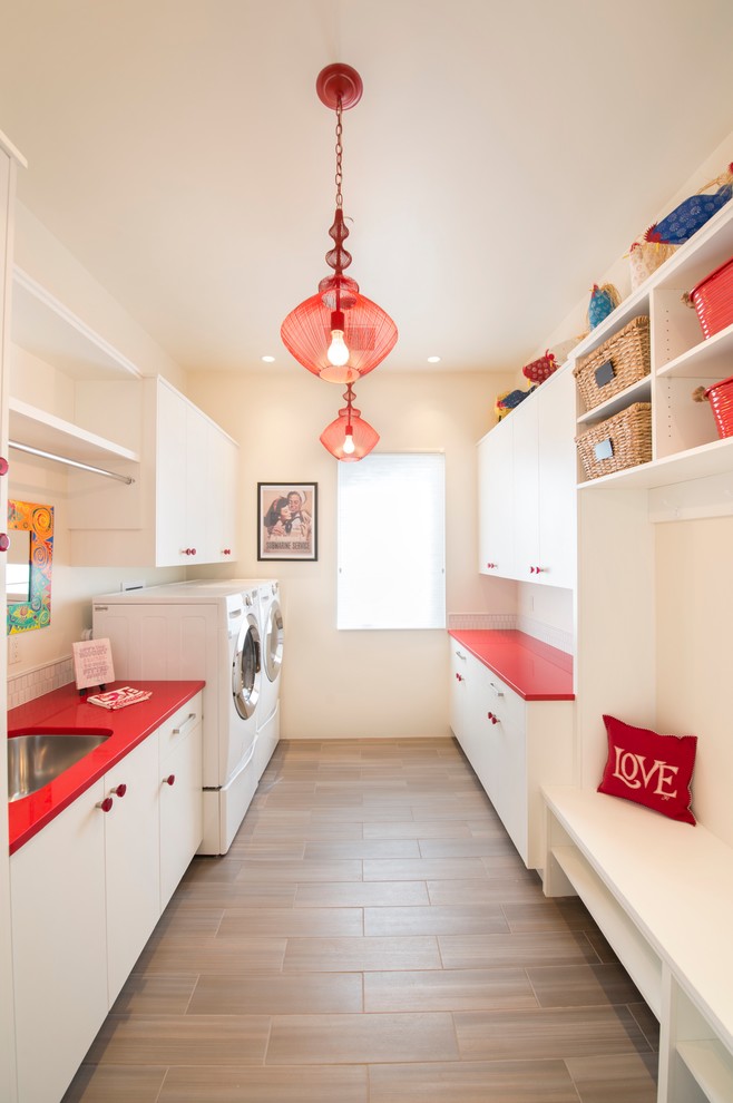 アルバカーキにある広いコンテンポラリースタイルのおしゃれな家事室 (ll型、アンダーカウンターシンク、フラットパネル扉のキャビネット、白いキャビネット、ベージュの壁、磁器タイルの床、左右配置の洗濯機・乾燥機、茶色い床、赤いキッチンカウンター) の写真