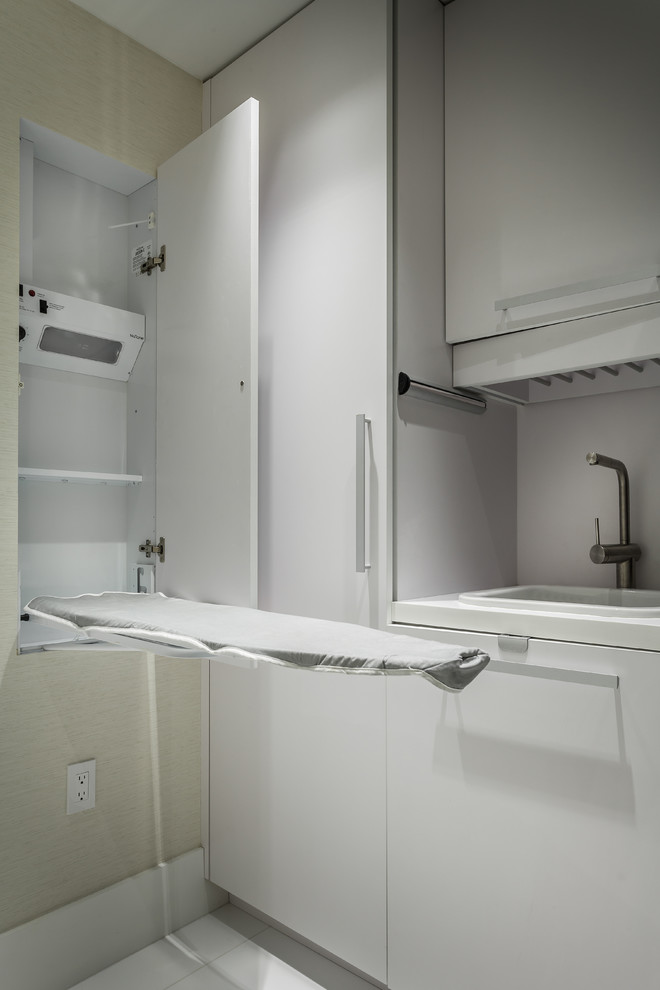 Photo of a small contemporary single-wall utility room in Miami with a built-in sink, flat-panel cabinets, white cabinets, quartz worktops, white walls, a stacked washer and dryer, porcelain flooring and white floors.