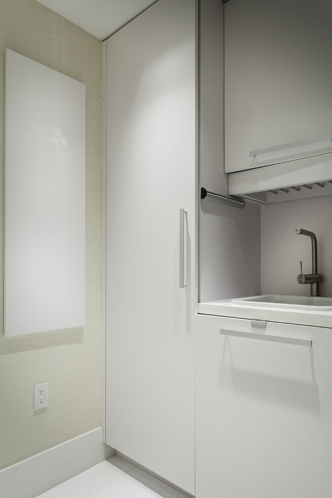 Design ideas for a small contemporary single-wall utility room in Miami with a built-in sink, flat-panel cabinets, white cabinets, quartz worktops, white walls, a stacked washer and dryer, porcelain flooring and white floors.