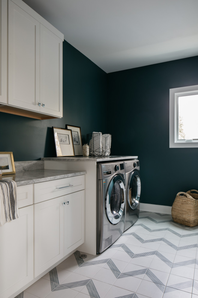Modelo de lavadero lineal tradicional renovado con armarios estilo shaker, puertas de armario blancas, paredes azules, lavadora y secadora juntas, suelo multicolor y encimeras grises
