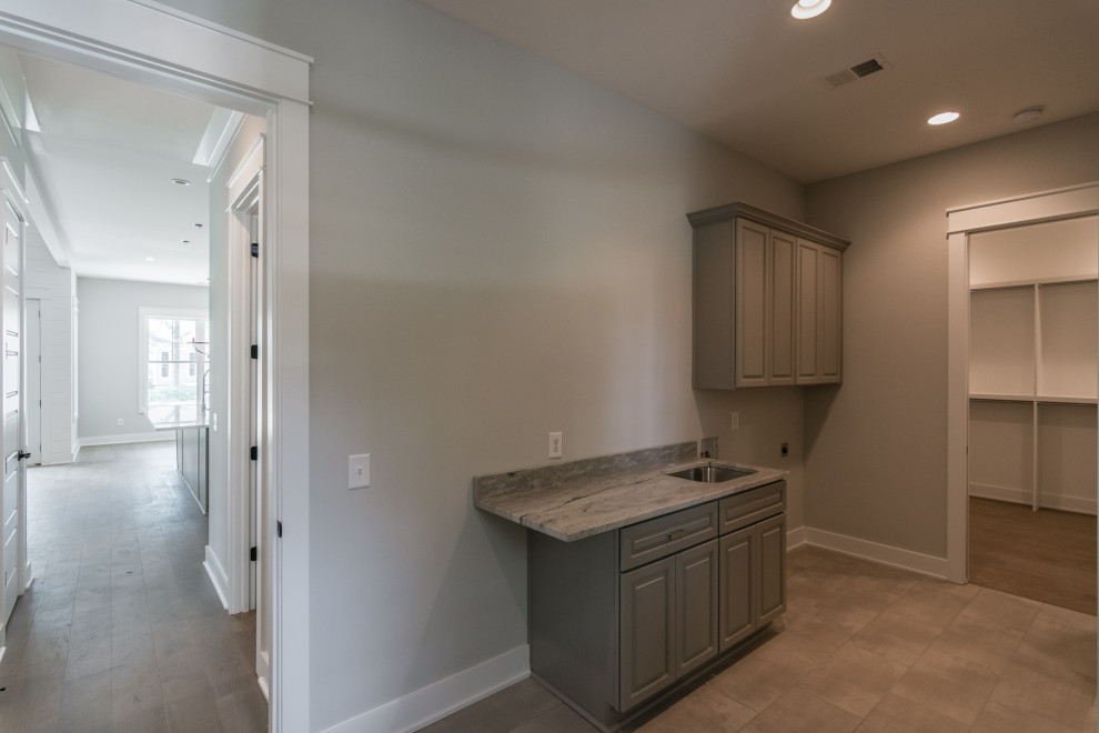 Mid-sized cottage single-wall porcelain tile and beige floor utility room photo in Nashville with an undermount sink, raised-panel cabinets, gray cabinets, granite countertops, gray walls, a side-by-side washer/dryer and gray countertops