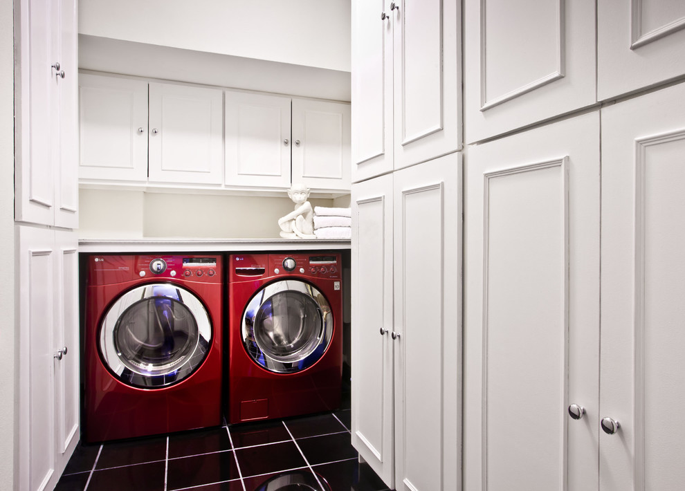 Diseño de lavadero tradicional renovado con puertas de armario blancas, lavadora y secadora juntas y suelo negro