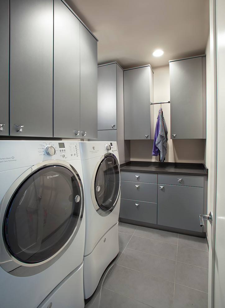 Modelo de lavadero en L actual con armarios con paneles lisos, puertas de armario grises, paredes beige y lavadora y secadora juntas
