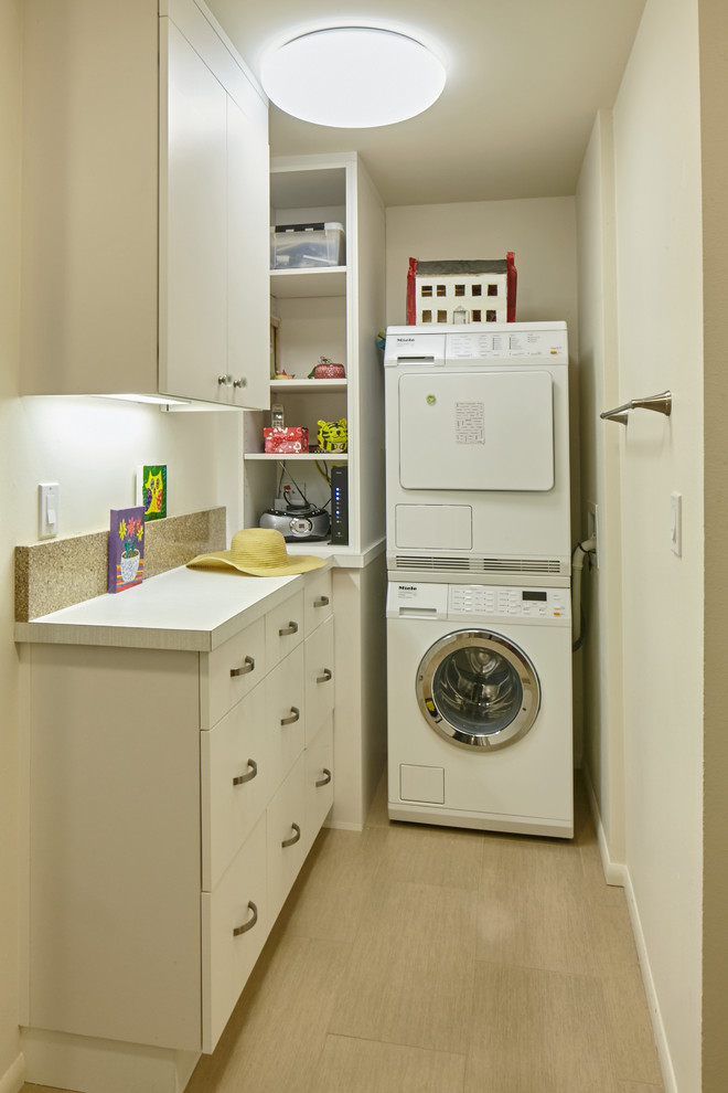 Imagen de cuarto de lavado en L contemporáneo pequeño con armarios con paneles lisos, puertas de armario blancas, encimera de laminado, paredes blancas, suelo de baldosas de porcelana y lavadora y secadora apiladas