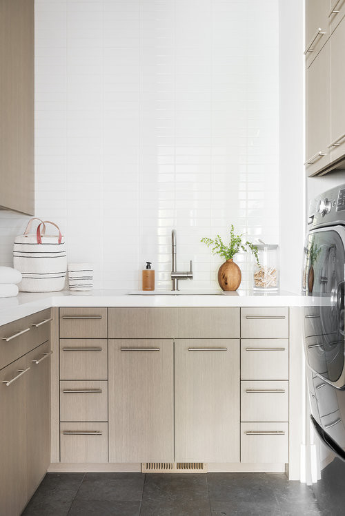Idee per una sala lavanderia minimalista di medie dimensioni con ante in legno chiaro, pareti bianche, pavimento con piastrelle in ceramica, lavatrice e asciugatrice affiancate, pavimento grigio e top bianco