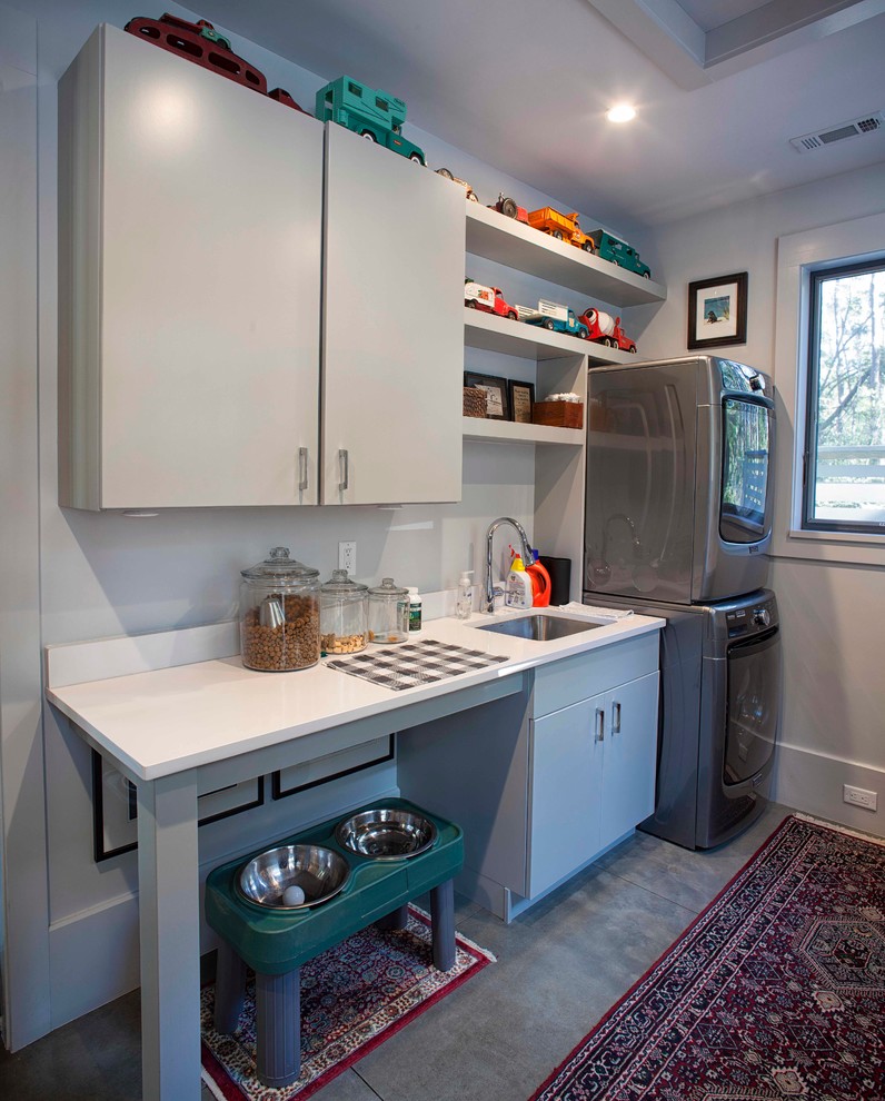 Example of a mid-sized trendy concrete floor dedicated laundry room design in Atlanta with an undermount sink, flat-panel cabinets, gray cabinets, quartz countertops, gray walls and a stacked washer/dryer