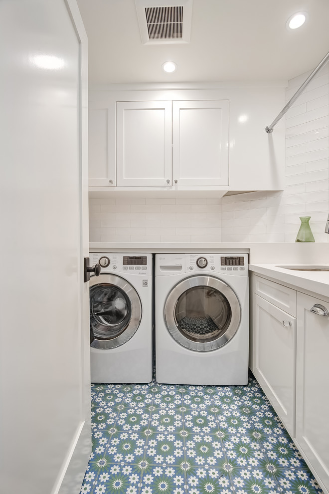 Klassische Waschküche in L-Form mit Unterbauwaschbecken, Schrankfronten im Shaker-Stil, weißen Schränken, weißer Wandfarbe, Waschmaschine und Trockner nebeneinander und buntem Boden in Orange County