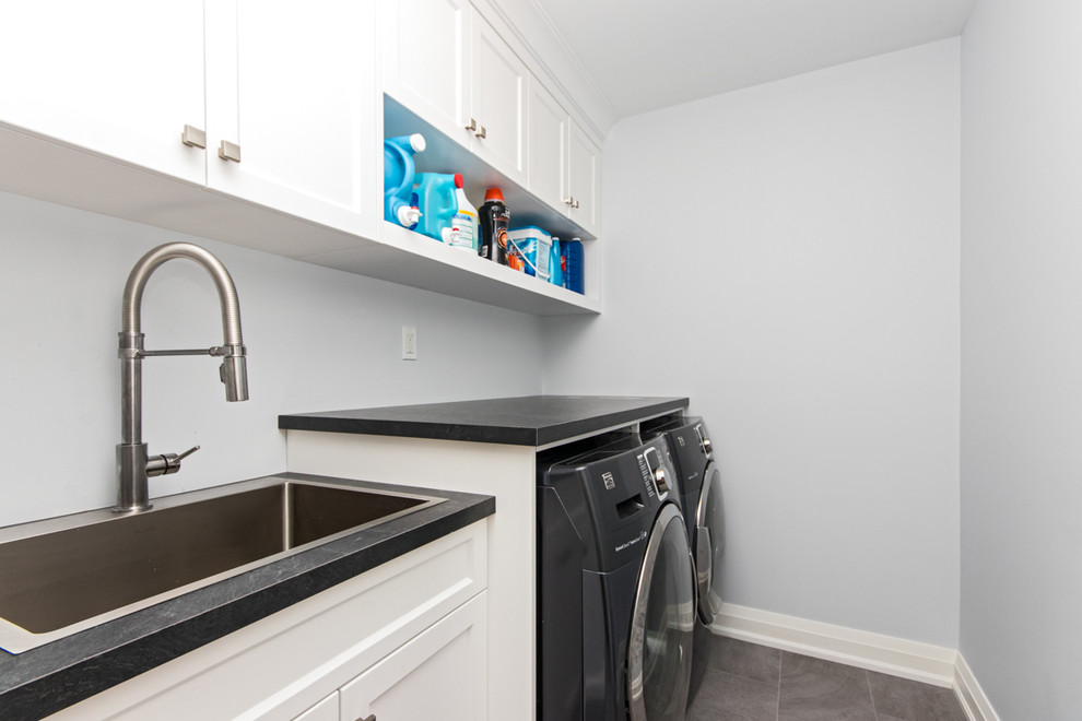 Inredning av en mellanstor grå parallell grått tvättstuga enbart för tvätt, med en nedsänkt diskho, skåp i shakerstil, vita skåp, laminatbänkskiva, grå väggar, klinkergolv i keramik, en tvättmaskin och torktumlare bredvid varandra och grått golv