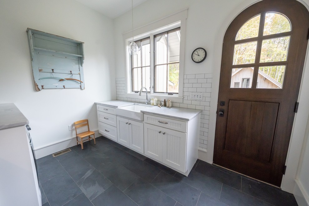 Bild på en lantlig parallell tvättstuga, med en rustik diskho, släta luckor, vita skåp, vita väggar, skiffergolv och blått golv